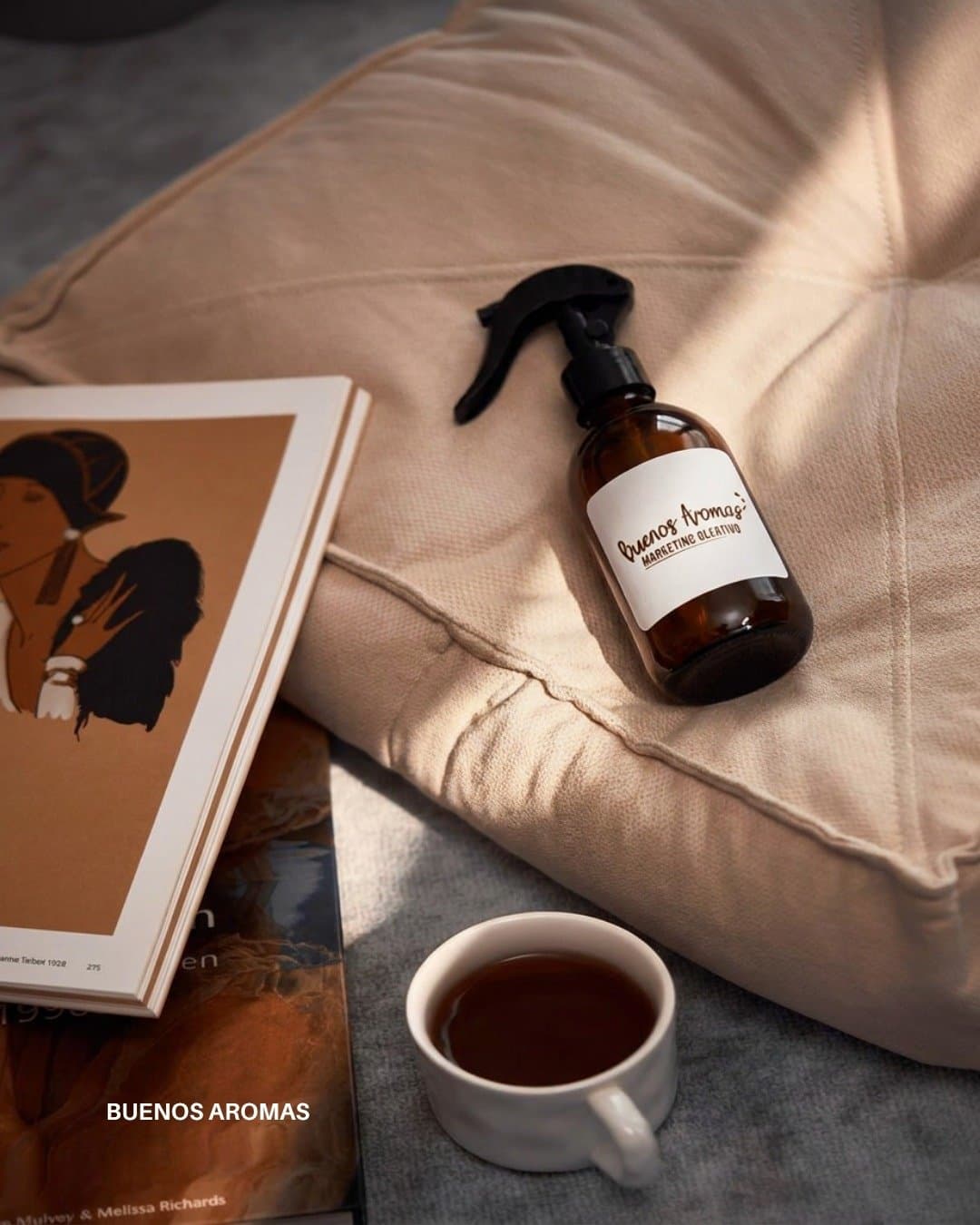 Home spray de vidrio ámbar sobre un almohadón, junto a una taza de té